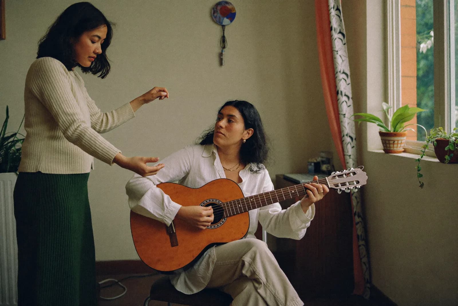 Escena ficticia generada de una profesora acompañando a una alumna adulta durante una clase de guitarra.